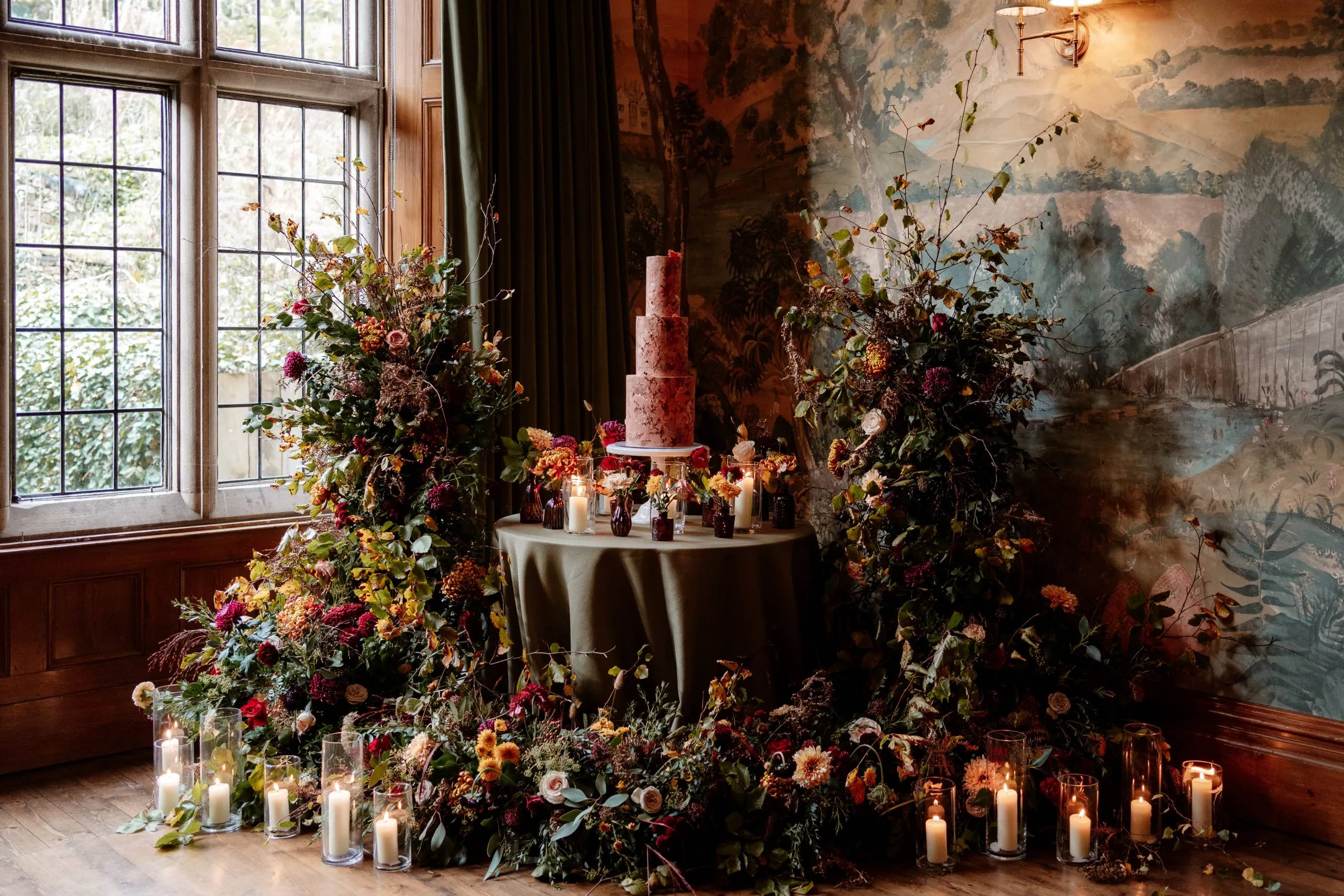 A four-tier cake framed by two tall autumn floral installations and candles