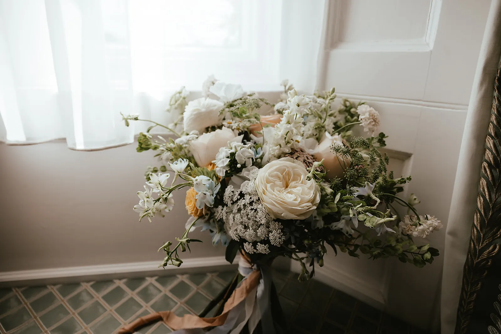 A white and green bridal bouquet by a window at Dunston Hall