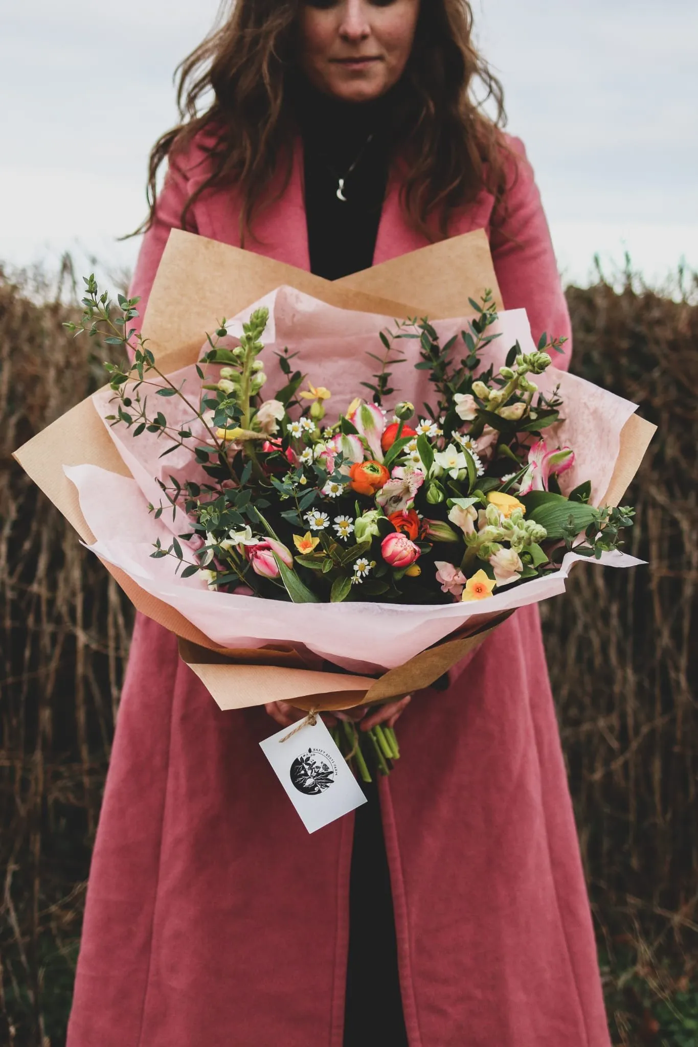 A wrapped seasonal bouquet held in a pink coat