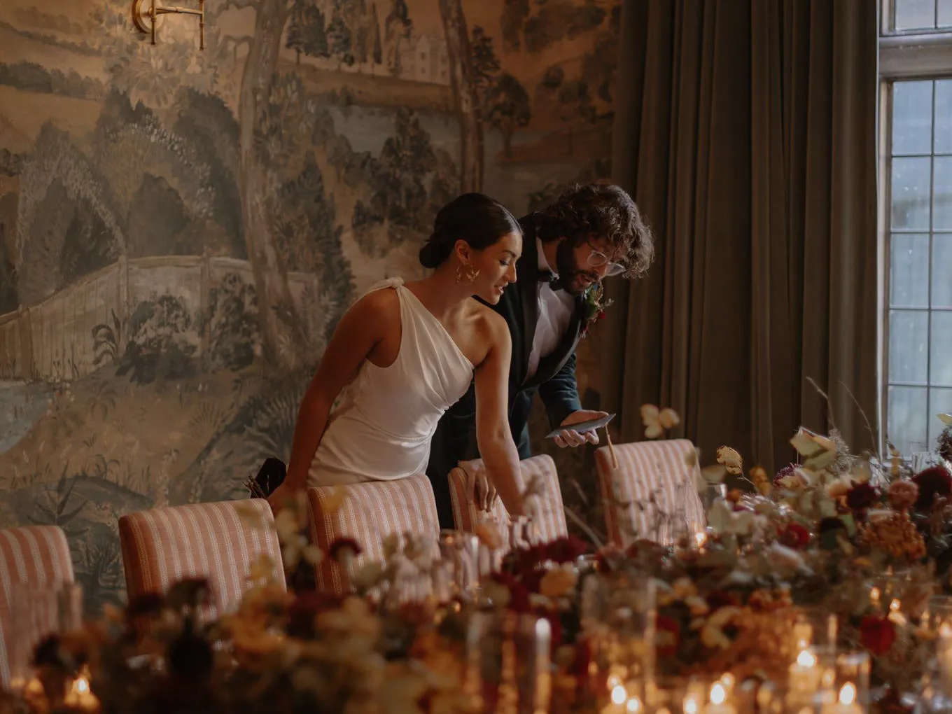 A couple leaning over a candlelit table of seasonal flowers