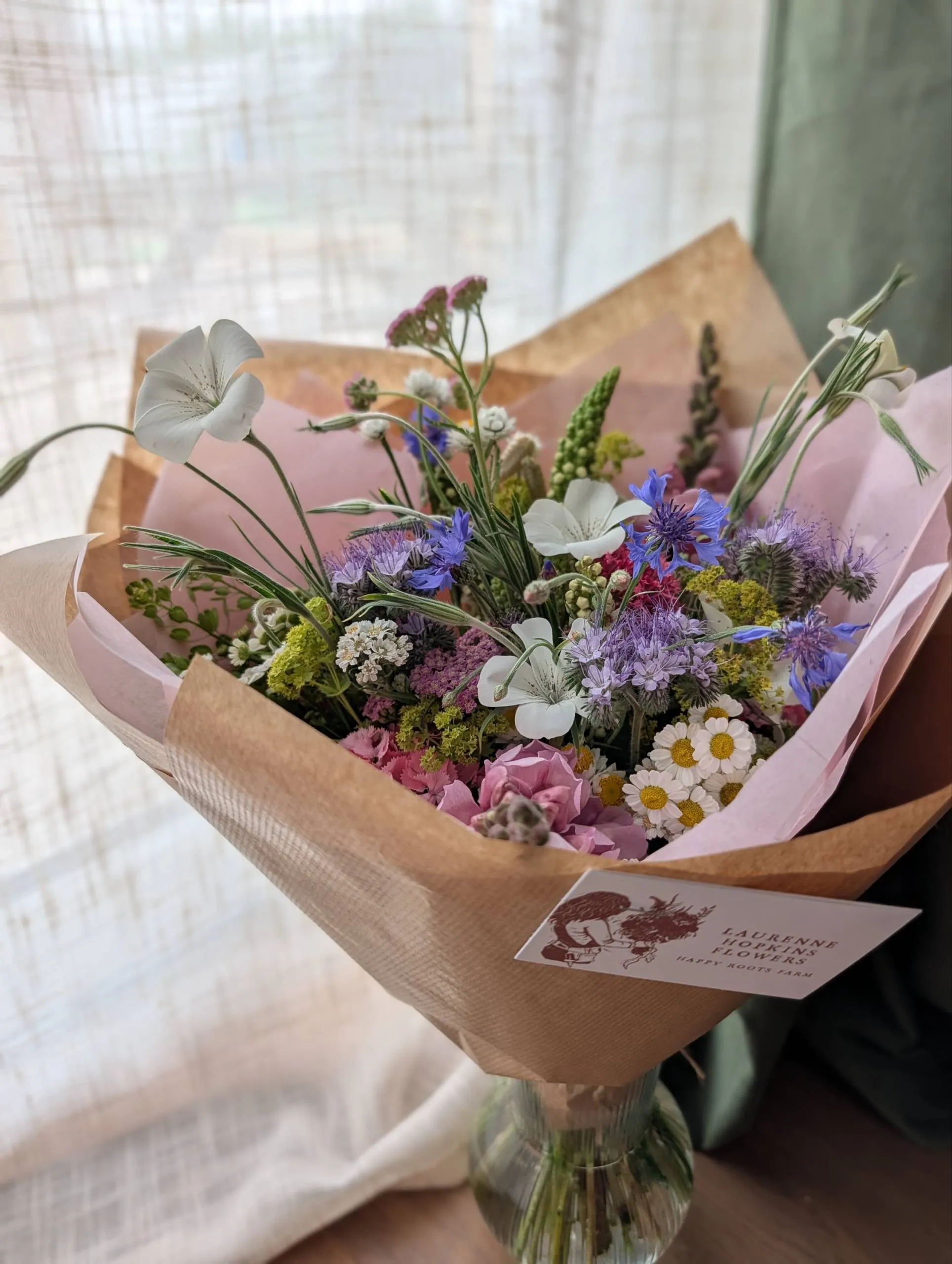 A wrapped cottage-garden bouquet in tissue and brown paper