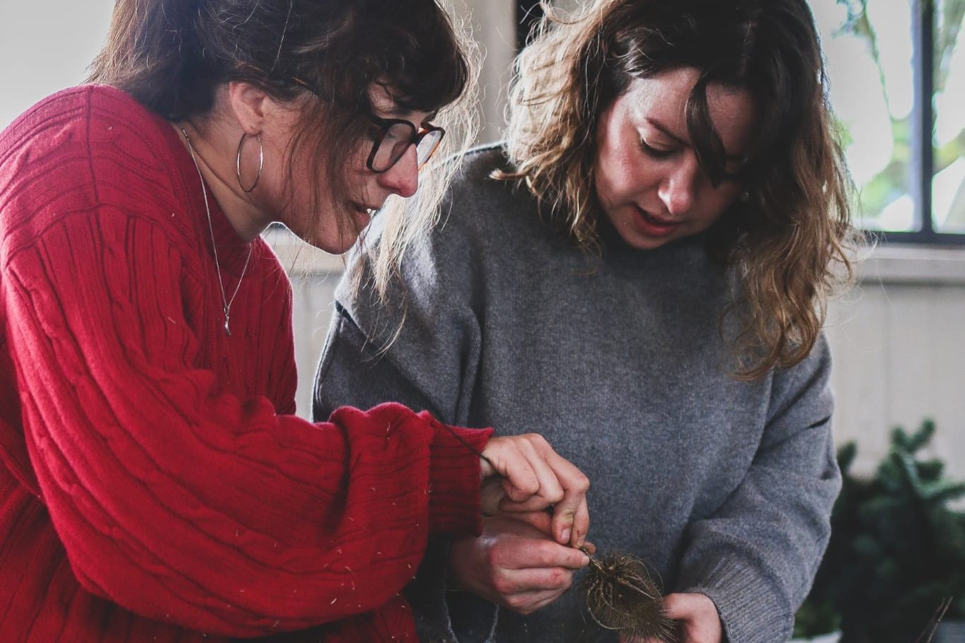 Two people making a Christmas wreath, with fairy lights overhead