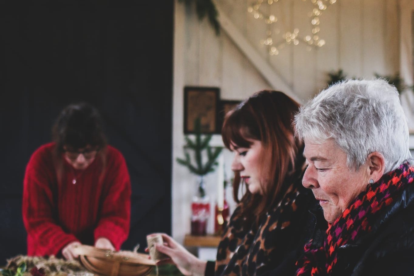 Hands wiring greenery into a Christmas wreath, with fairy lights